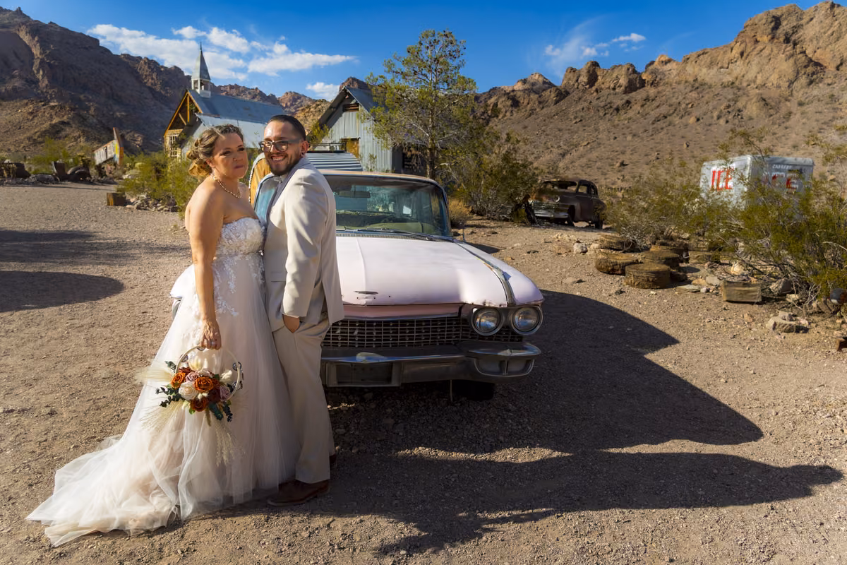 Newlyweds posing beside a vintage pink Cadillac at Nelson Ghost Town