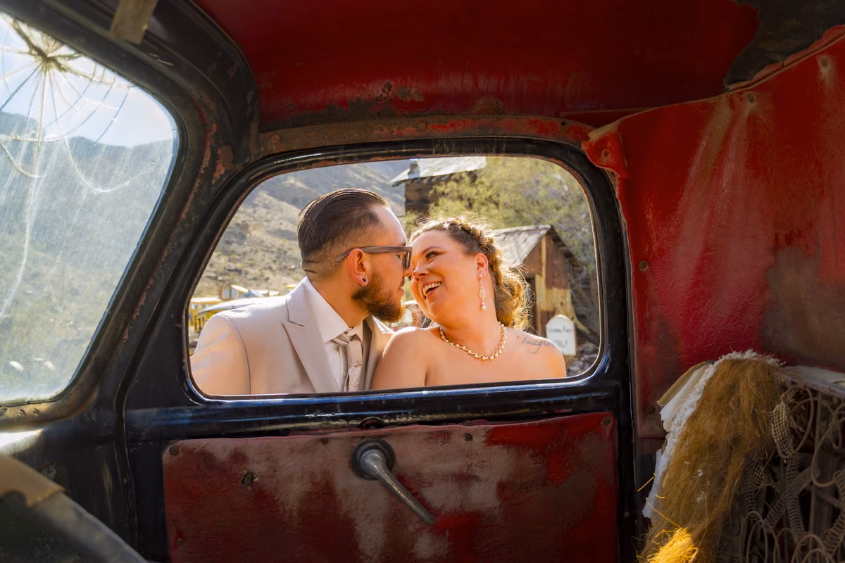 Newlyweds framed by the window of a vintage red truck at Nelson Ghost Town